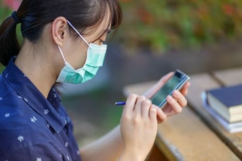 woman wearing health mask while using smartphone