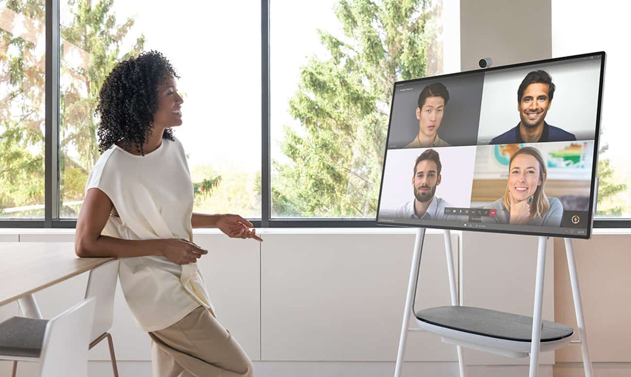 woman casually speaking with four workers over video on a surface hub 2s