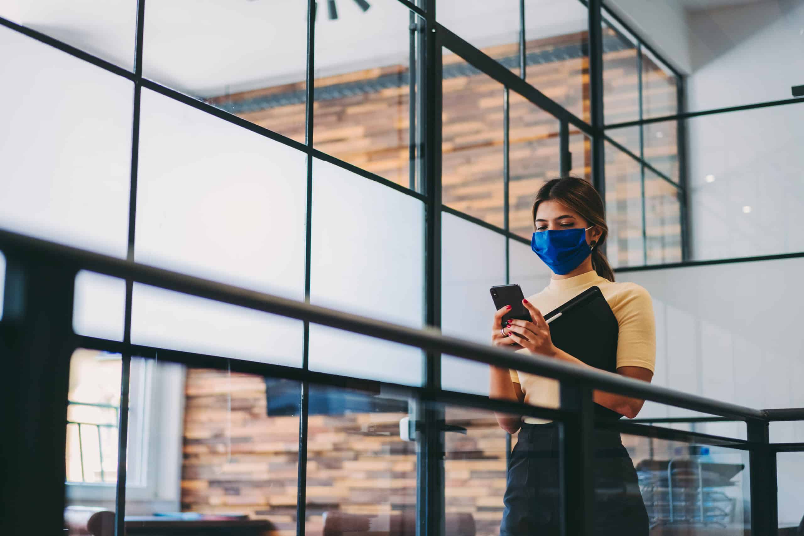 woman wearing mask using mobile device in a productive hybrid workplace