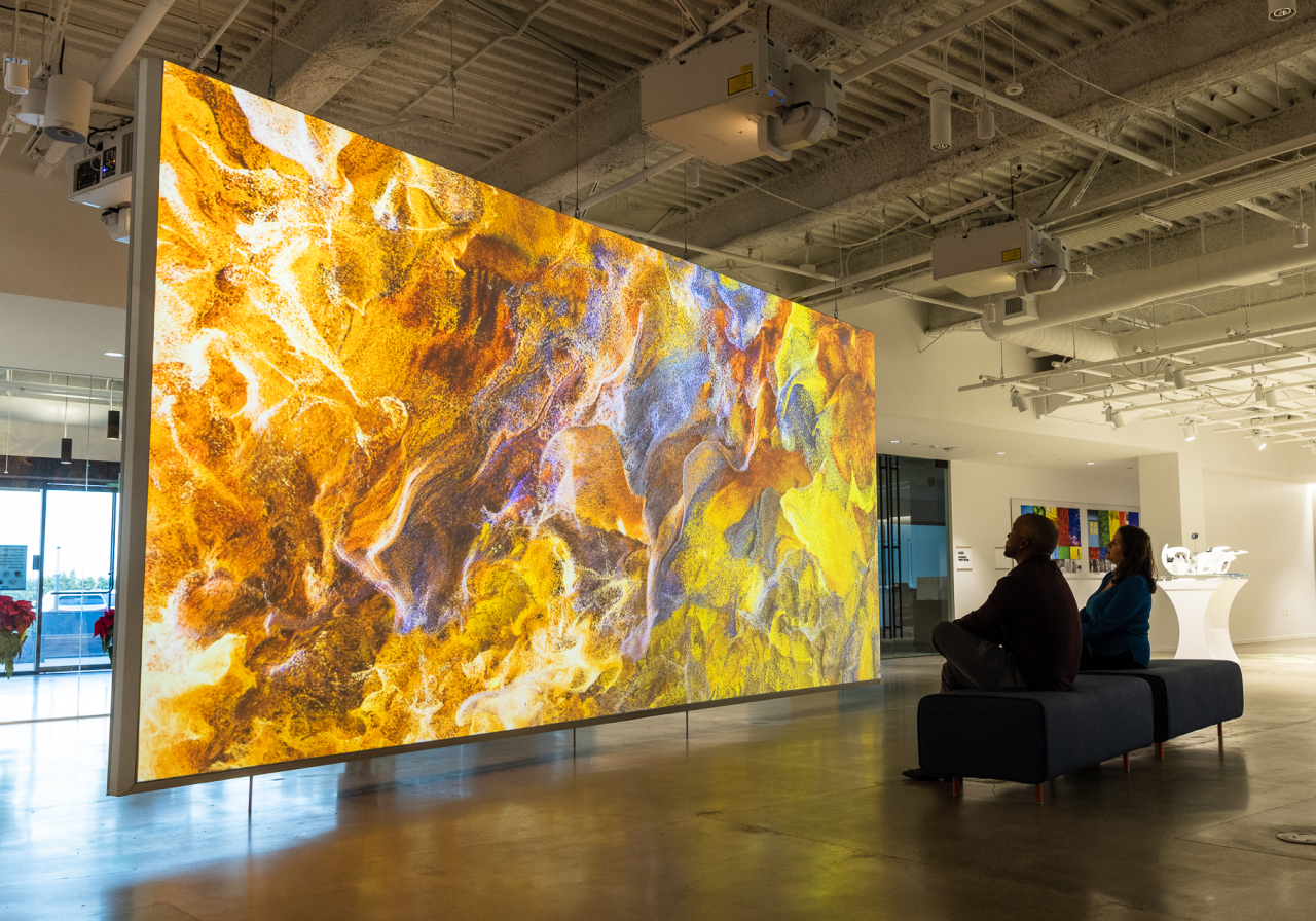 Large digital display with swirling abstract patterns observed by two people in a modern gallery.