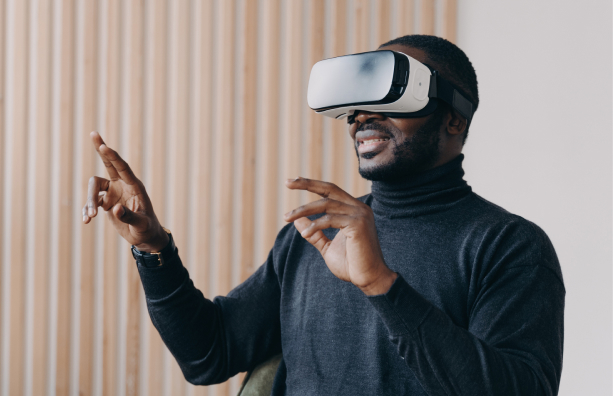 A person wearing a virtual reality headset gestures with both hands, appearing engaged. They are seated in front of a wooden panel wall and wearing a dark turtleneck sweater.