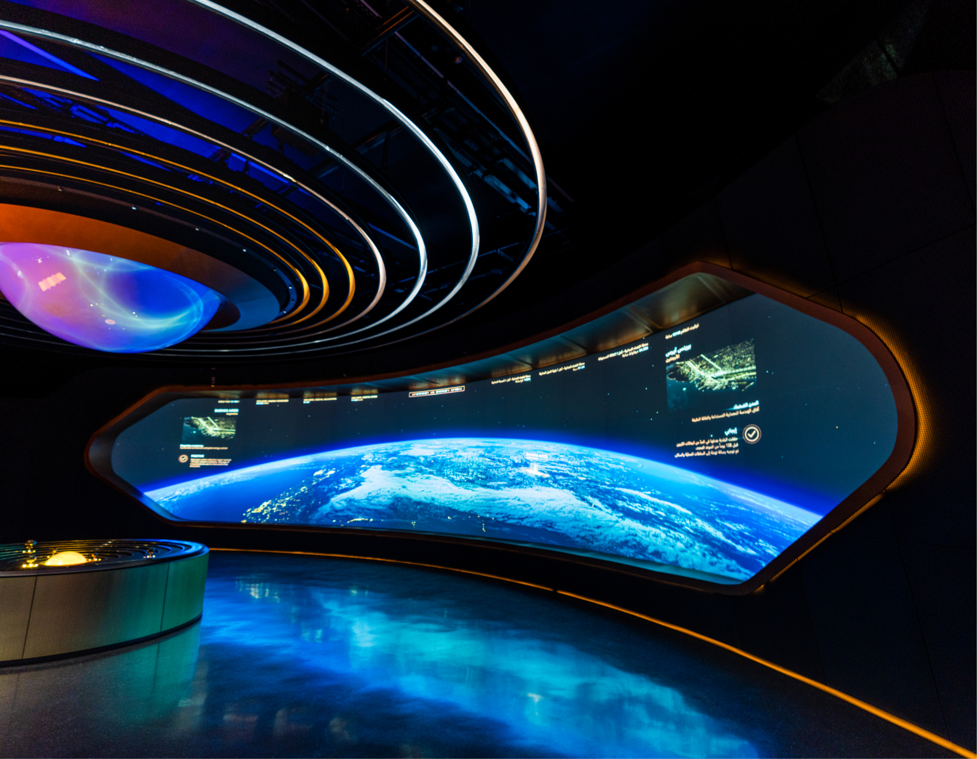 Futuristic room: large curved screen shows Earth from space. Circular console on the left, blue lighting, concentric ceiling rings.