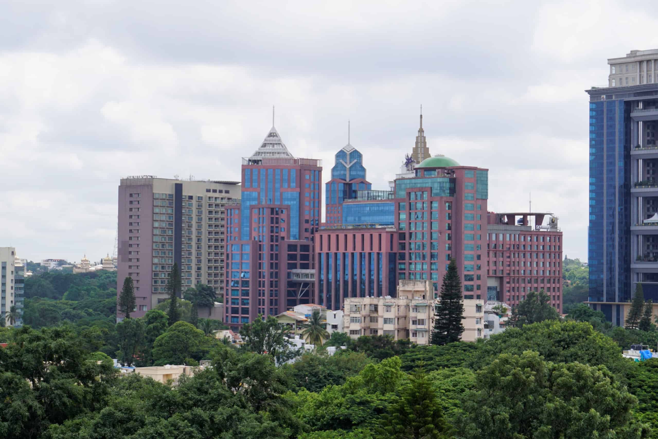 A cityscape with modern skyscrapers and lush greenery under a cloudy sky.