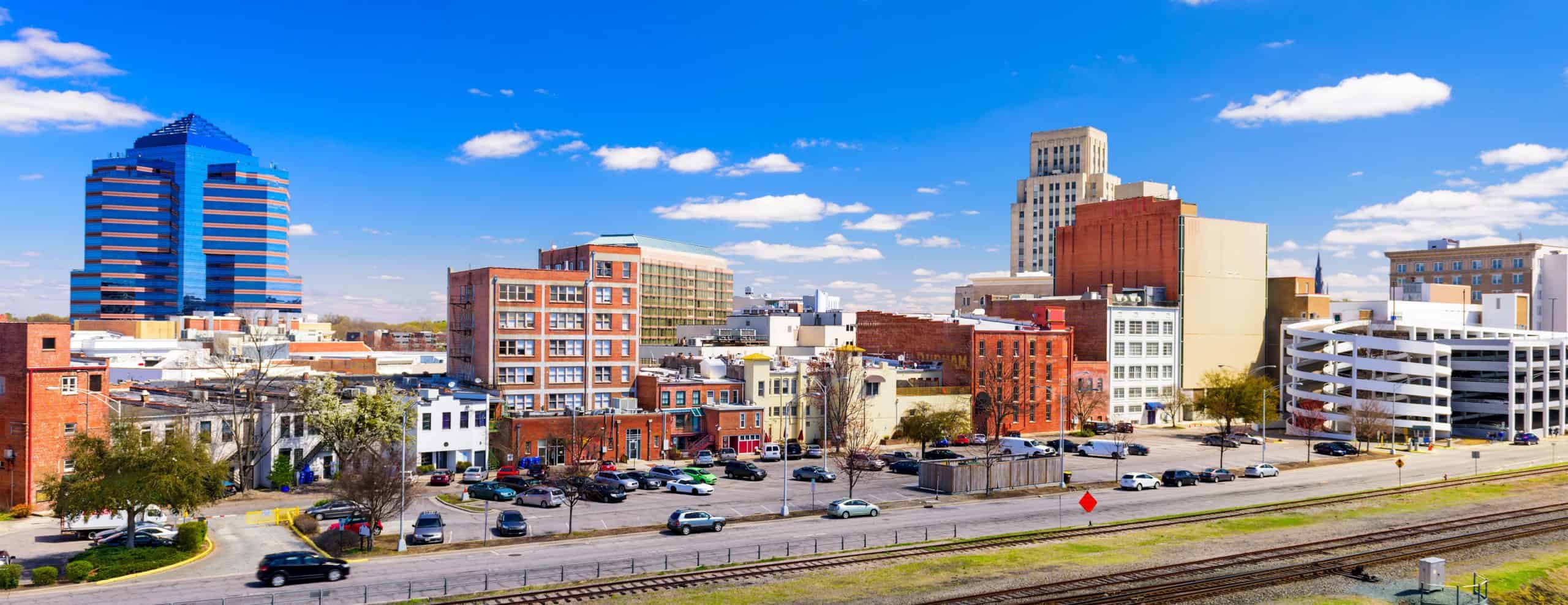 Modern and historic cityscape with skyscrapers, brick buildings, parking, and railway under a blue sky with scattered clouds.