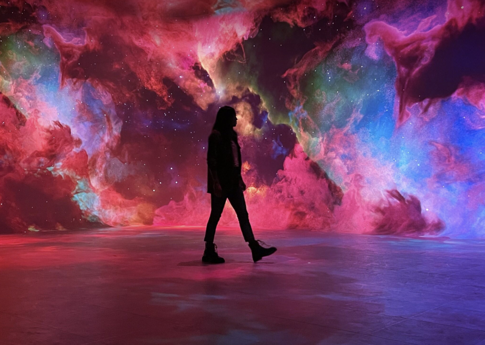 Silhouette of a person walking in front of vivid cosmic swirls of red, pink, blue, and green nebulae, creating a dream-like scene.