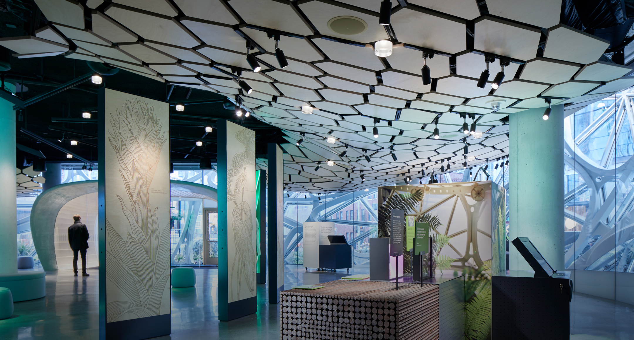 Modern interior with geometric ceiling, nature-themed decor; leaf panels & interactive displays. Sunlight streams through glass.