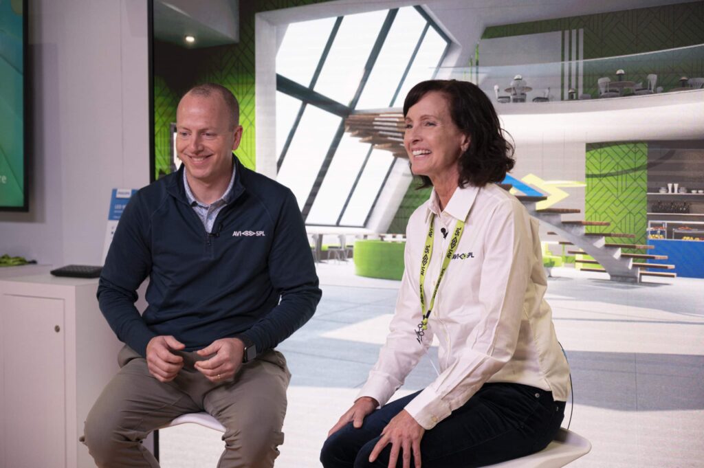 Two people on stools in a bright space, one in a dark jacket, the other in a white shirt. Theyre smiling and engaged in chat.