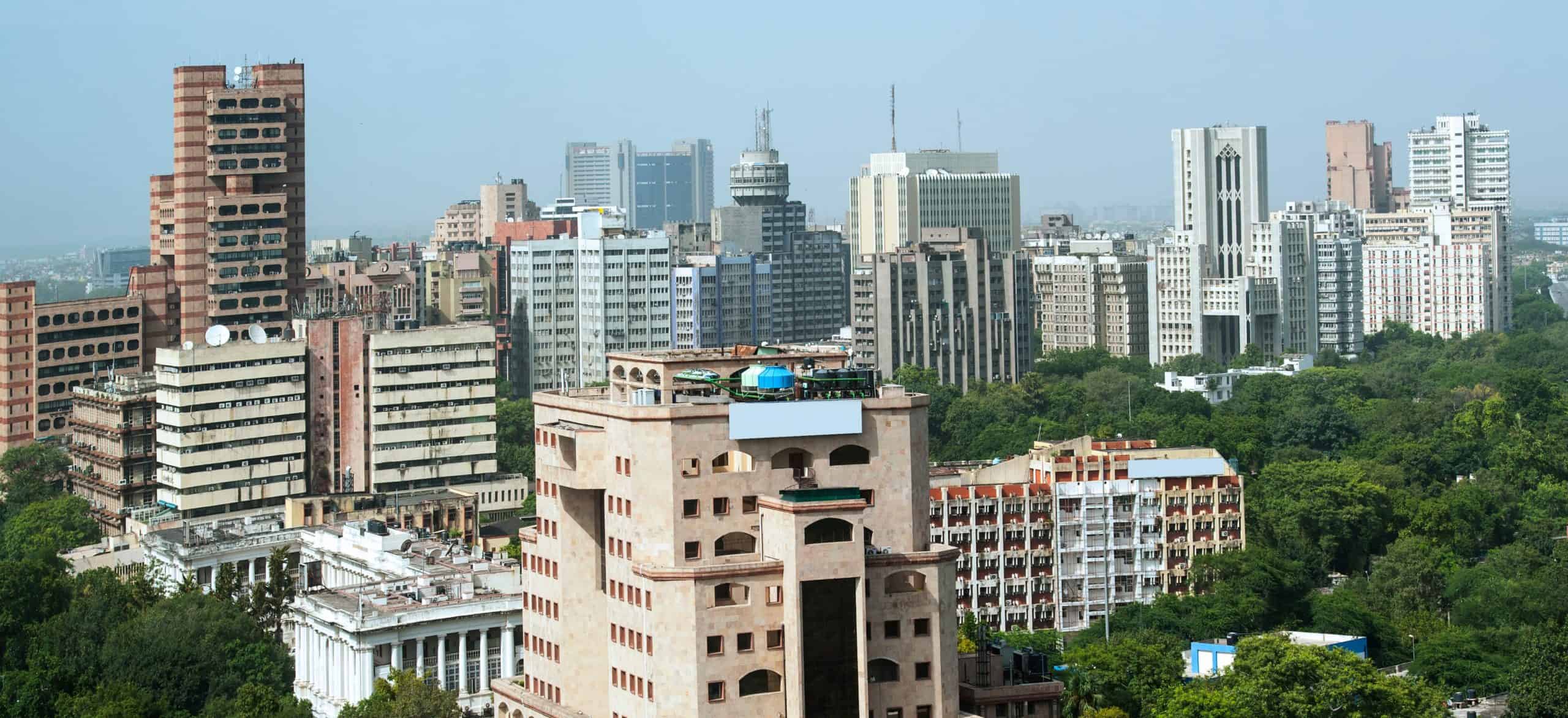 City skyline with modern high-rises, old structures, greenery; clear sky enhances urban view.