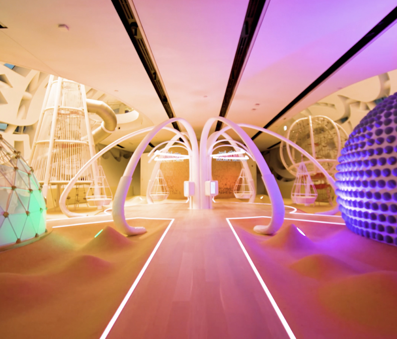 Curved white structures, neon pink/purple lights, smooth wood floor; dome shapes & arches create a sci-fi vibe.