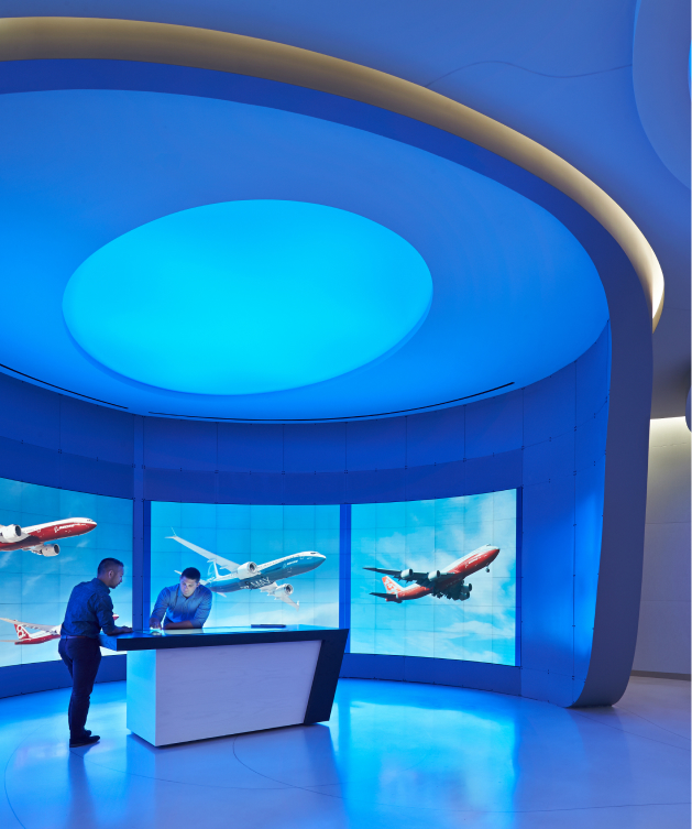 Two people at a sleek desk in a modern room with blue lighting; screens show planes flying. High-tech, professional ambiance.