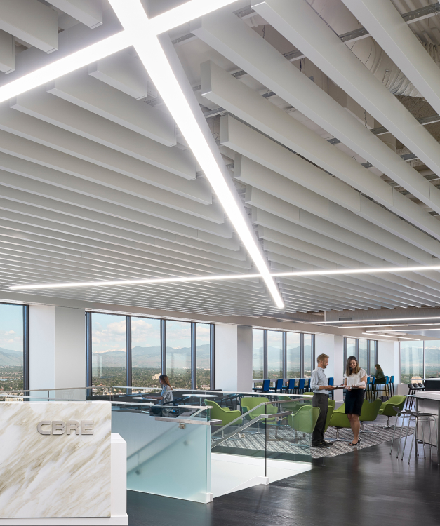 Modern office with city view, two people talking by a glass railing, green chairs, white beams, LED lights; CBRE visible.