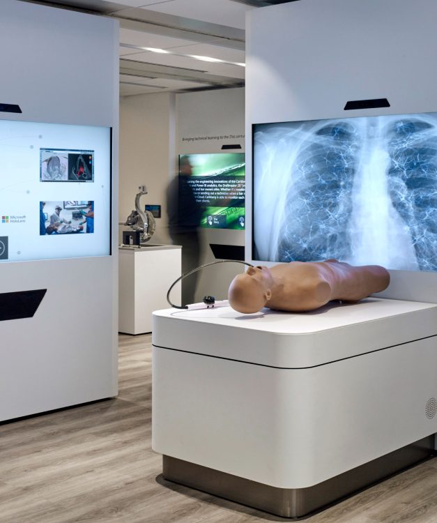 A medical exhibit features a digital screen with chest X-rays, a mannequin on a white platform, and sleek futuristic design elements.