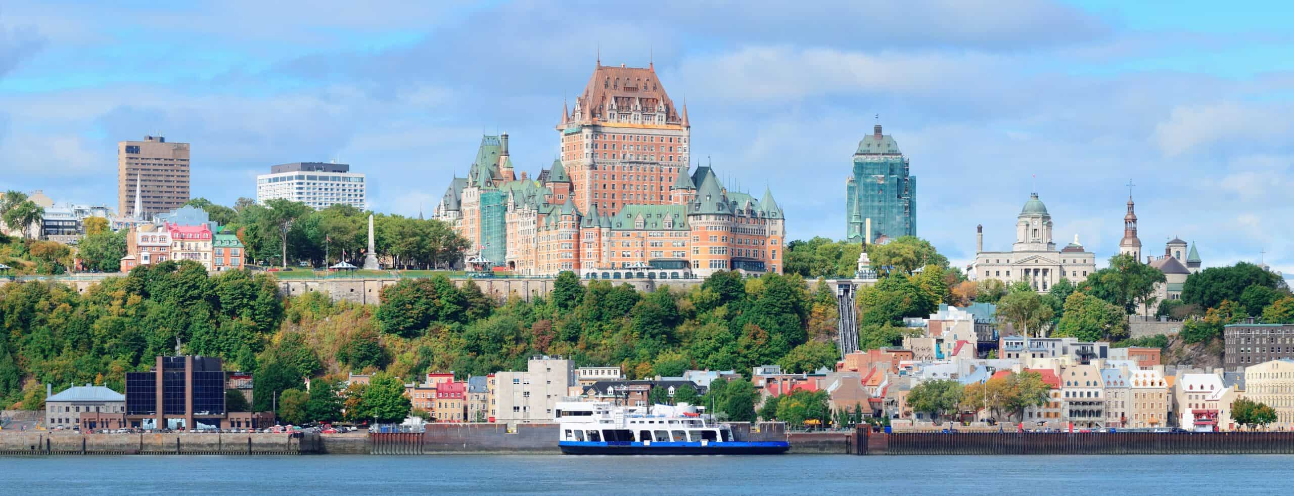 Quebec City with Château Frontenac centered, historic buildings around, a ferry on the St. Lawrence River, partly cloudy sky.