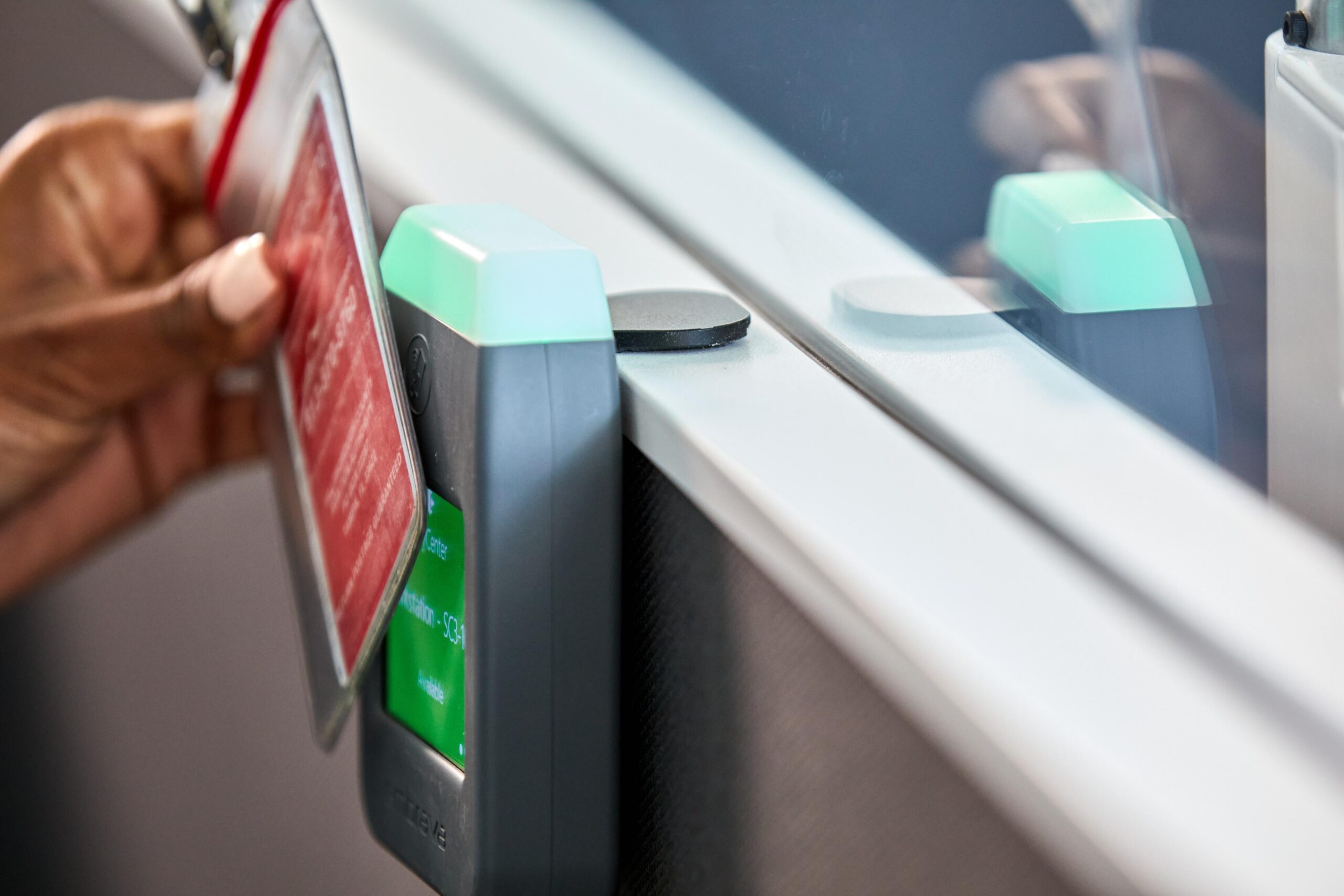 Hand holds a red card near train station scanner, green light signals access. Focus: hand and scanner.