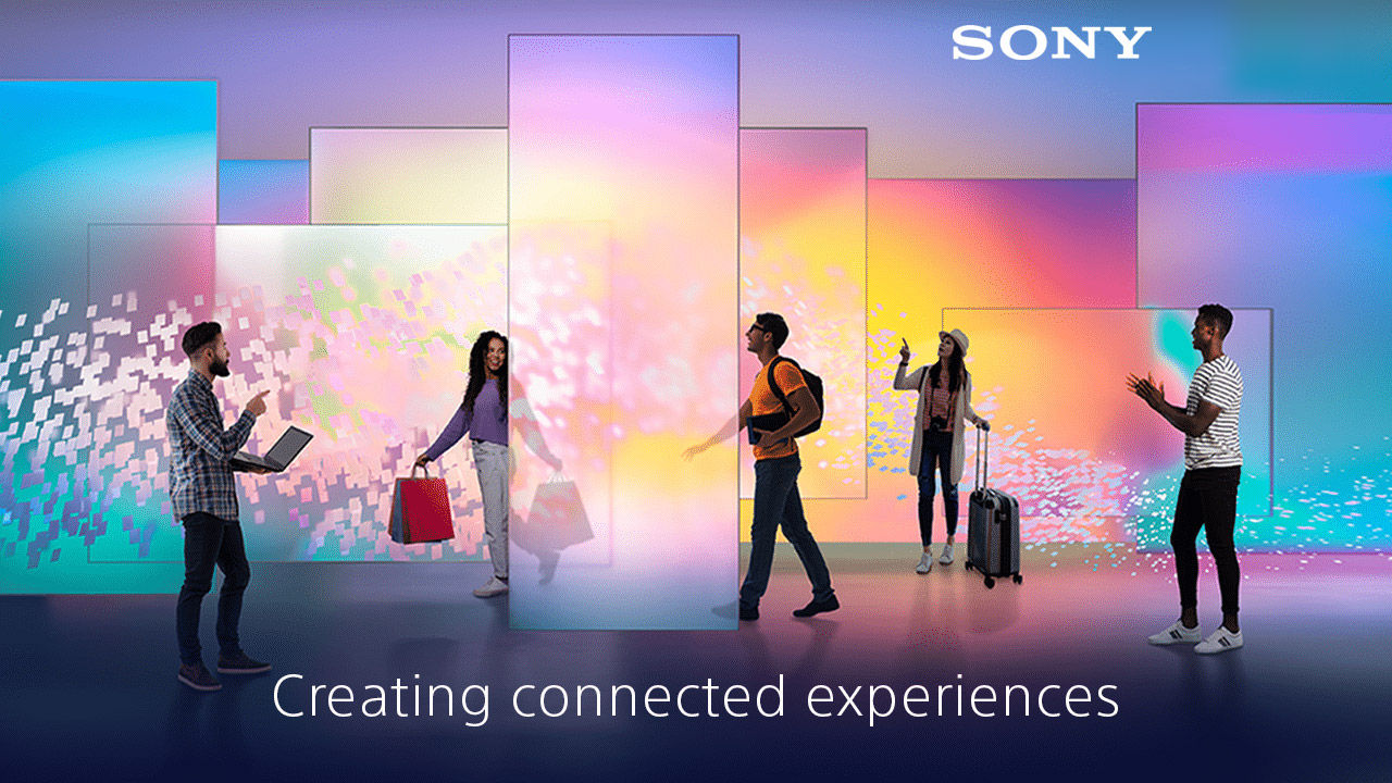 People stand before a vibrant, digital backdrop with screens; one holds a laptop, others have shopping bags and a suitcase. Sony: Creating connected experiences.