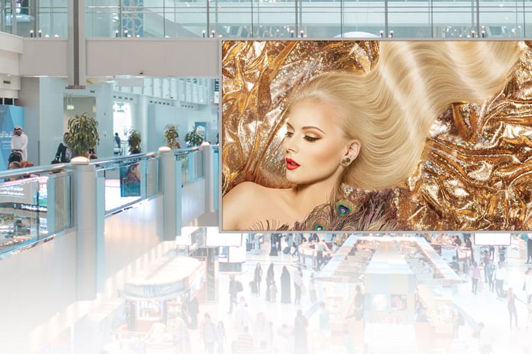 Ad: Glamorous woman with long blonde hair on gold backdrop in bustling, modern mall.