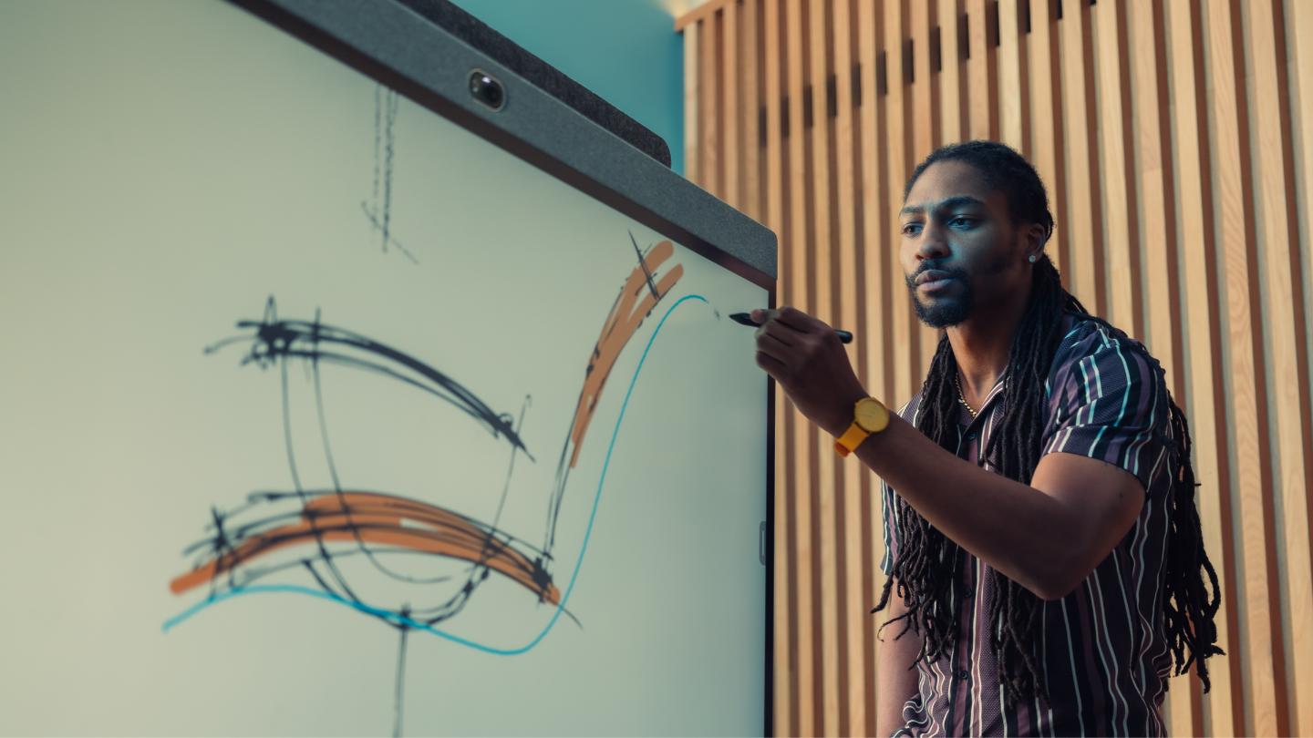 Person with long hair uses a stylus on a large screen displaying abstract lines. Wooden paneled wall in the background.