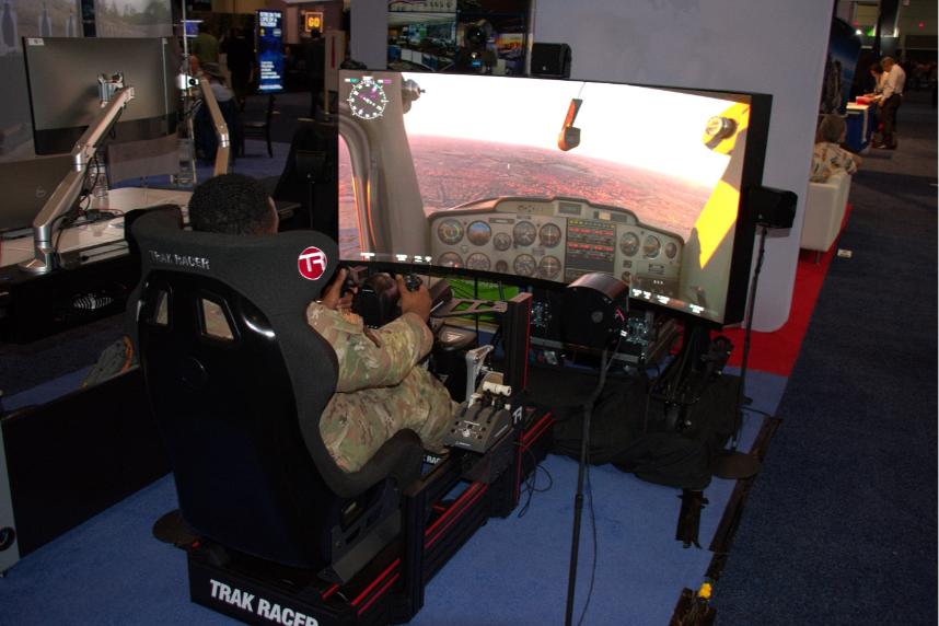 In a TRAK RACER seat, a person in uniform uses flight sim controls with a curved screen showing cockpit view.