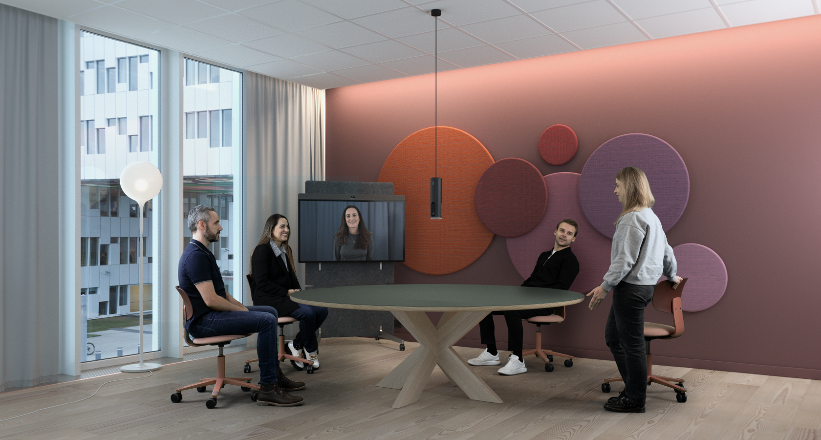 Four people in a meeting room: three seated, one standing by a round table. Woman joins via video call. Modern decor, large windows.