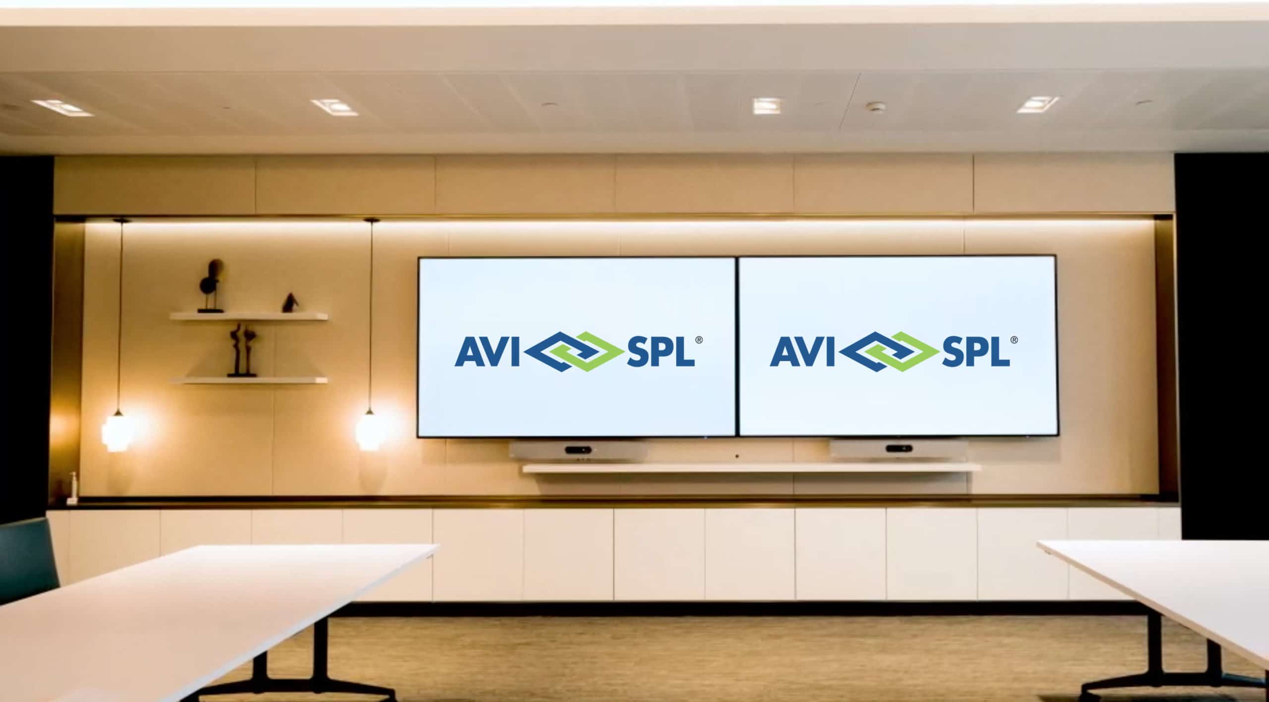 Modern conference room: two large screens with AVI-SPL logo, shelves with decor, long table & chairs, neutral tones, minimalist design.