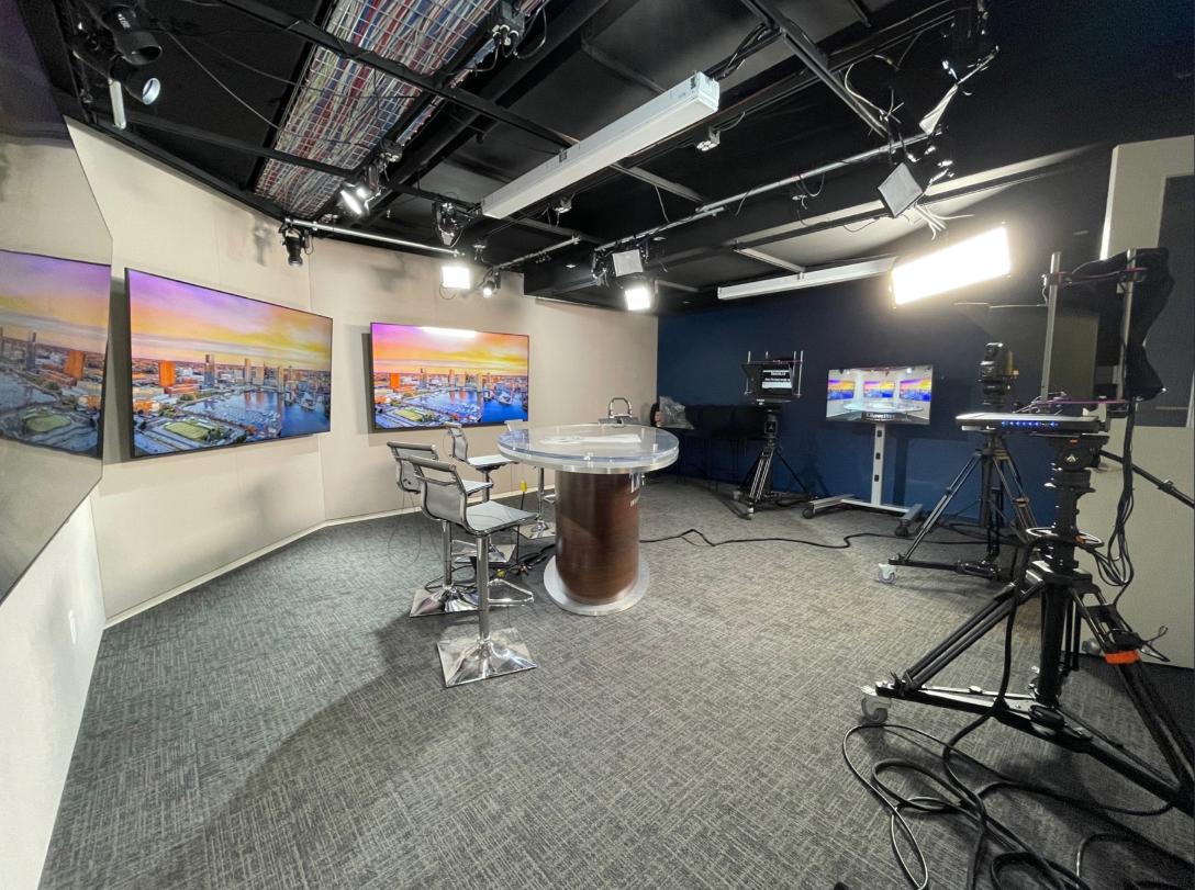 Modern TV studio with central news desk, 3 cityscape screens, several cameras, and bright lights highlighting sleek design.