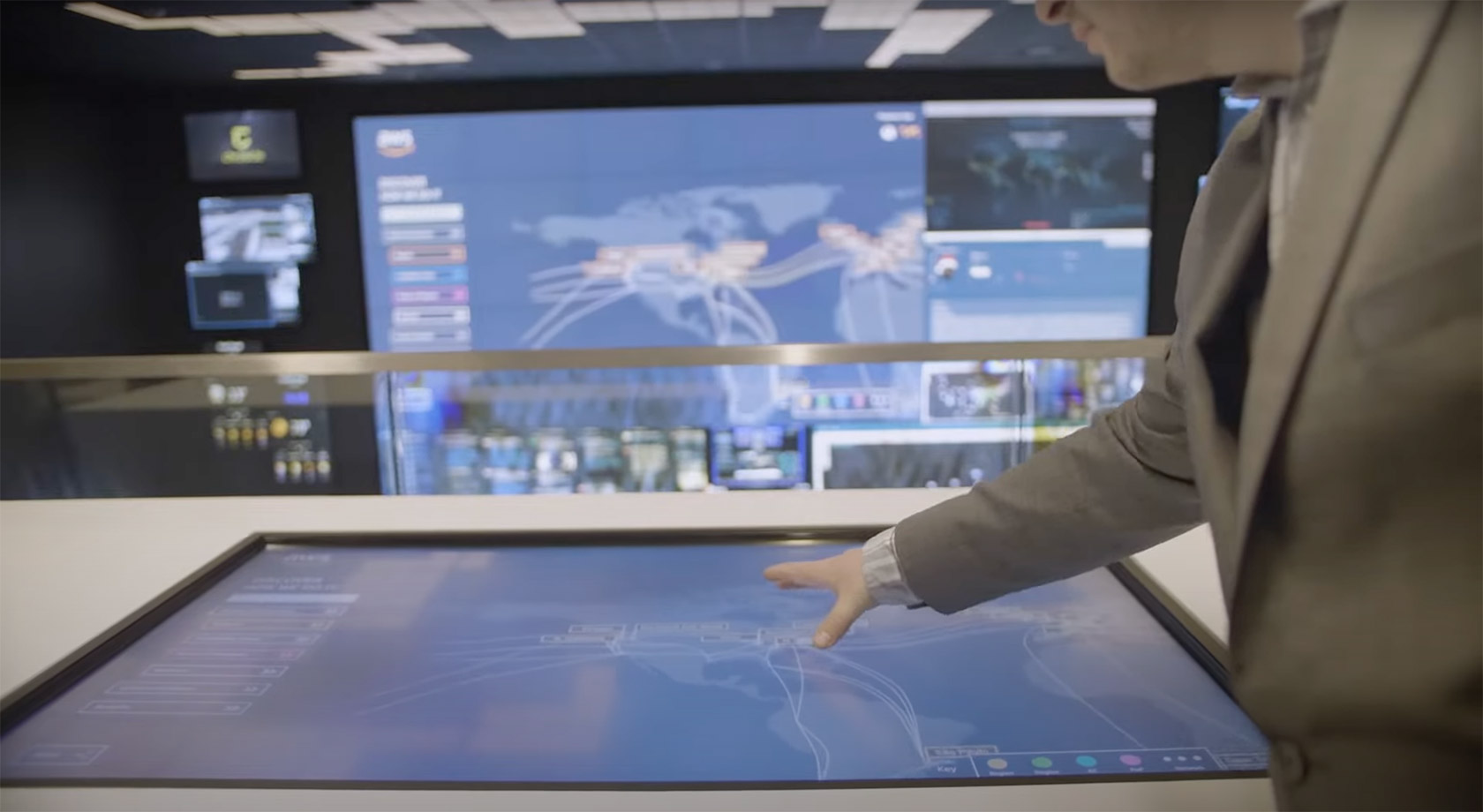 A suited person interacts with a large touchscreen in a high-tech Crestron control room, surrounded by digital maps and data screens.