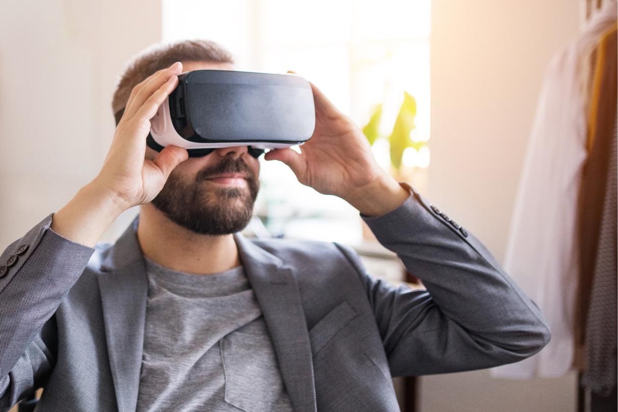 Man in gray suit and VR headset indoors, sunlight filters through the window.