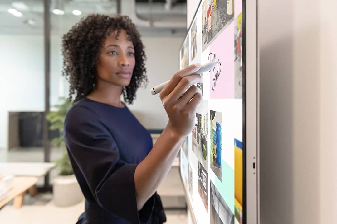 A curly-haired woman uses a stylus on a large touchscreen with images in a modern office, focused on the screen.