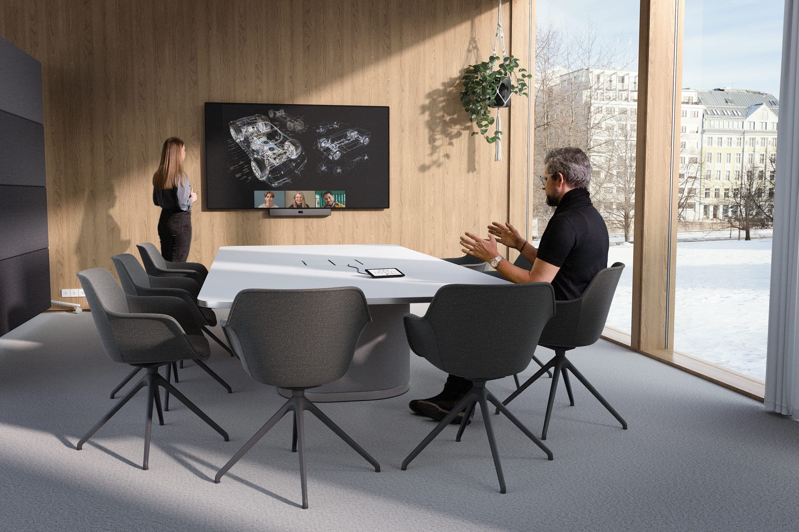 Woman by wall screen in conference room; man gesturing at table. Large windows reveal snowy landscape outside.