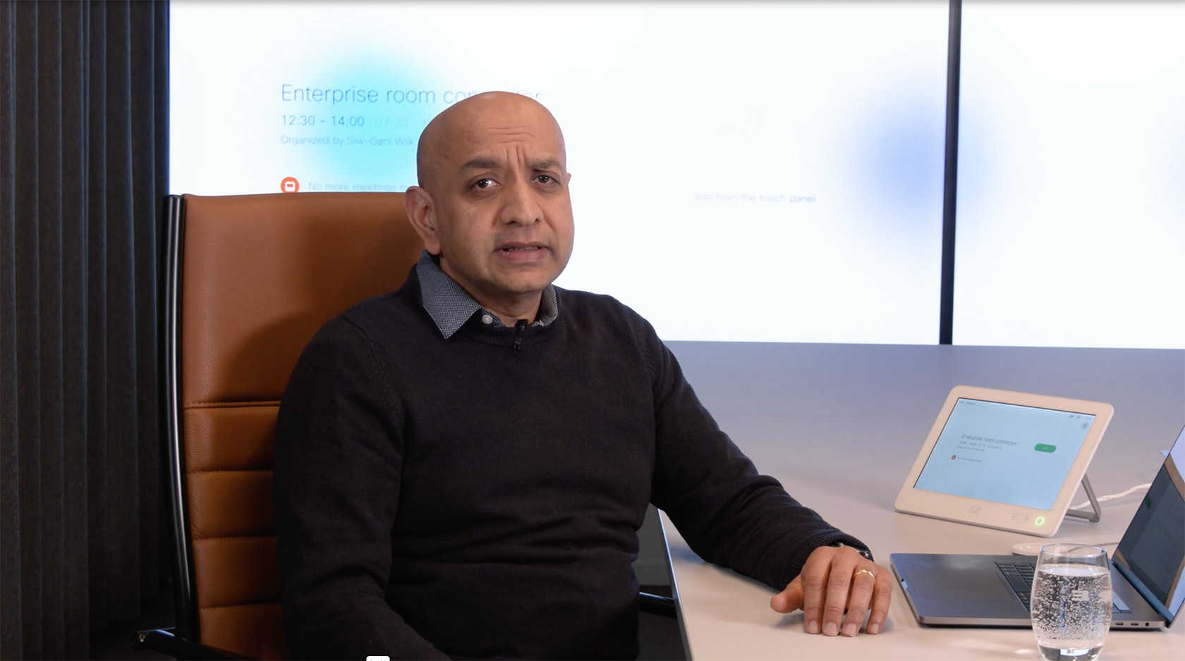 Man sat a meeting room table and talking to the camera.