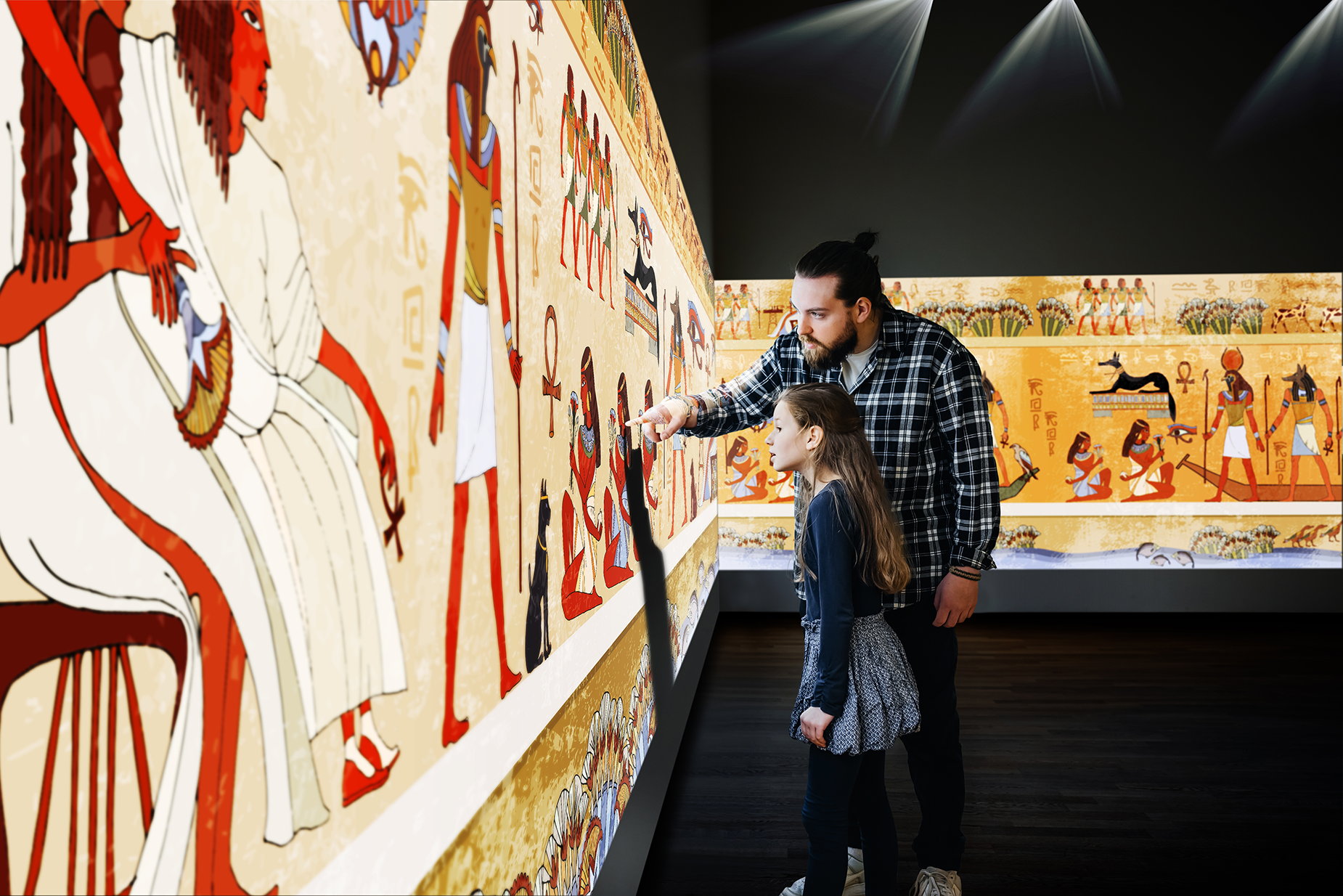 A father and his daughter look at and touch an immersive projection of Egyptian art.