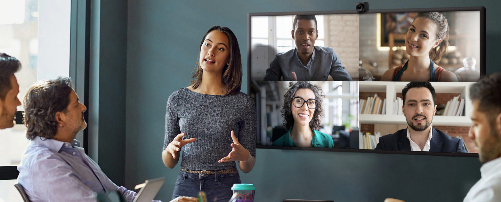 Woman standing in front a conference room display, leading a hybrid meeting.