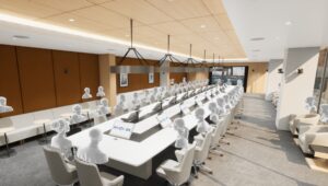 Extra-large conference room with a long table. Attendees have individual confidence monitors and microphones. Table faces a large wall-mounted display at the end of the room.