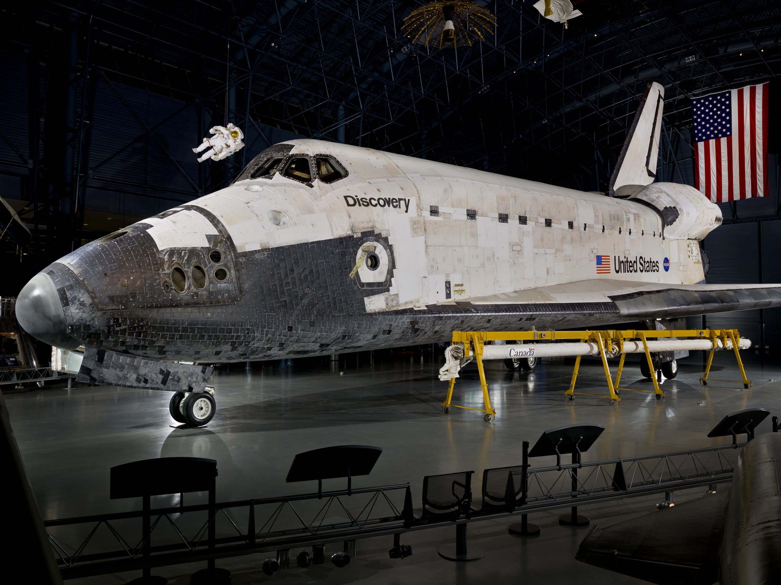 View of Space Shuttle Discovery (OV-103) (A20120325000) on display in the James S. McDonnell Space Hangar at the National Air and Space Museum's Steven F. Udvar-Hazy Center, May 3, 2012. The Shuttle Remote Manipulator Arm (SRMS, Canadarm) is displayed in the foreground, under the Shuttle's left wing and the MMU (Manned Maneuvering Unit) can be seen floating above the flight deck windows.