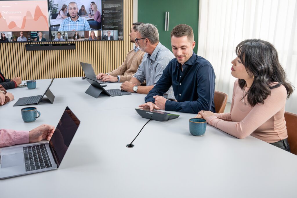 People in a conference room with Shure audio solutions and a video meeting on the display with remote attendees