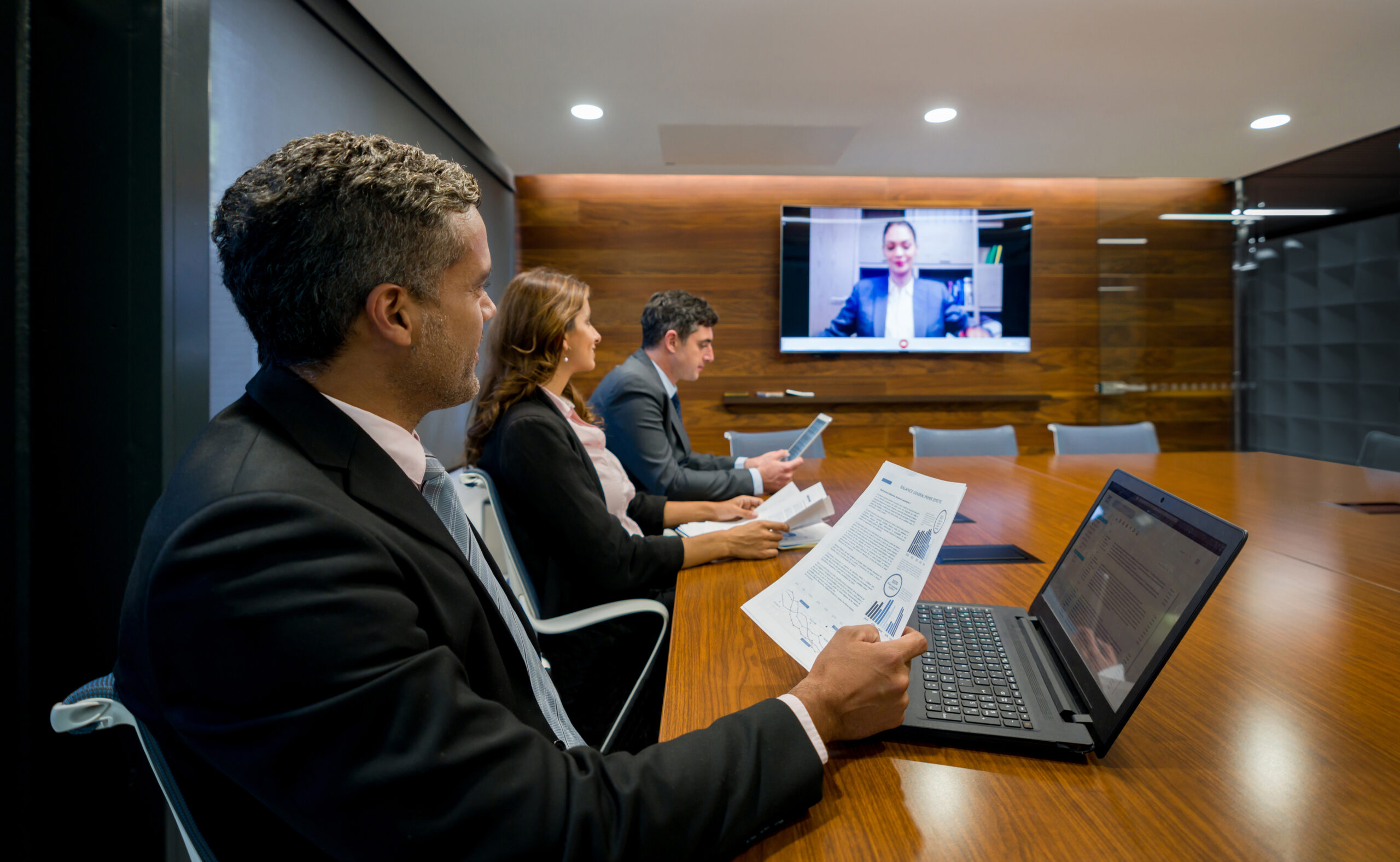 Three people sitting in a law firm meeting room with a video meeting on the display.