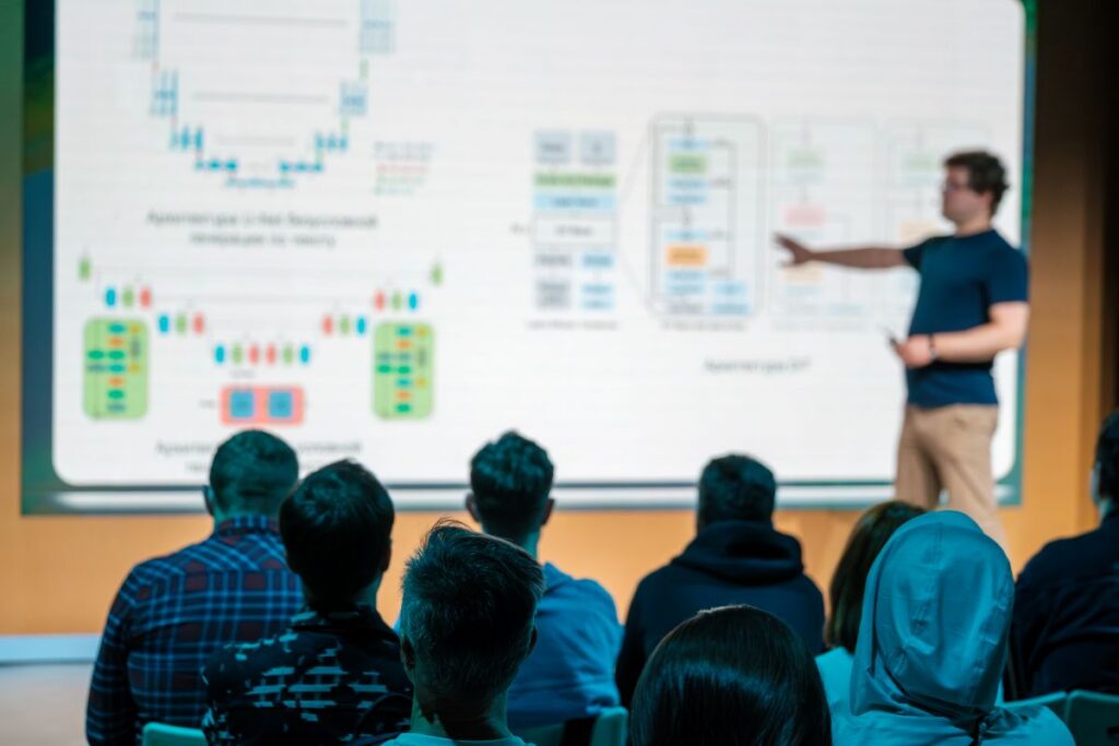 Students in a modern higher education classroom viewing course content on a large digital display as an instructor presents.